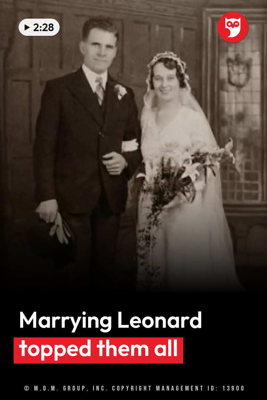 A man and a woman in formal clothes stand together indoors, holding flowers and a hat, posing for a photo. A headline runs in white letters across the lower third.