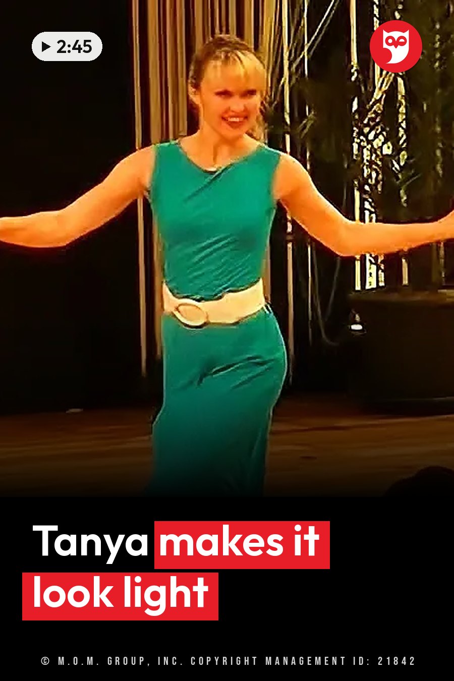 A woman in a green dress with a white belt stands on a stage, smiling, with her arms spread wide. A headline runs in white letters across the lower third.