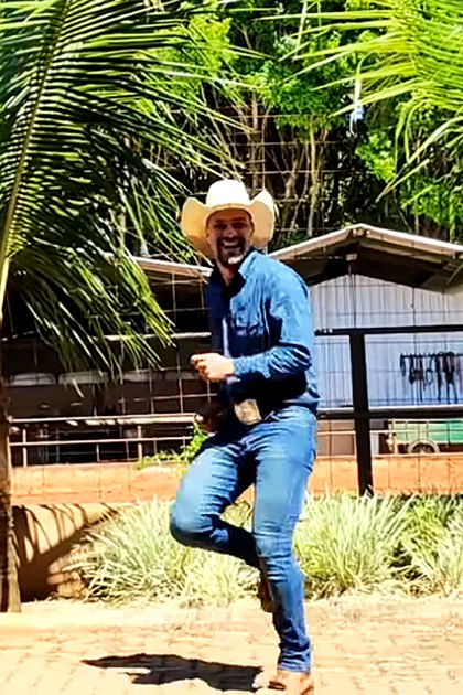 Three adult males in a tropical outdoor setting, wearing cowboy attire with palm trees and bright sunlight visible.