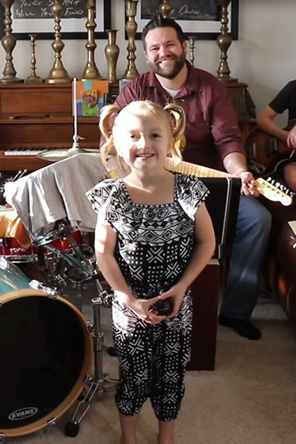 A cozy living room with a mix of vintage and modern decor elements, with children playing musical instruments and adults smiling.