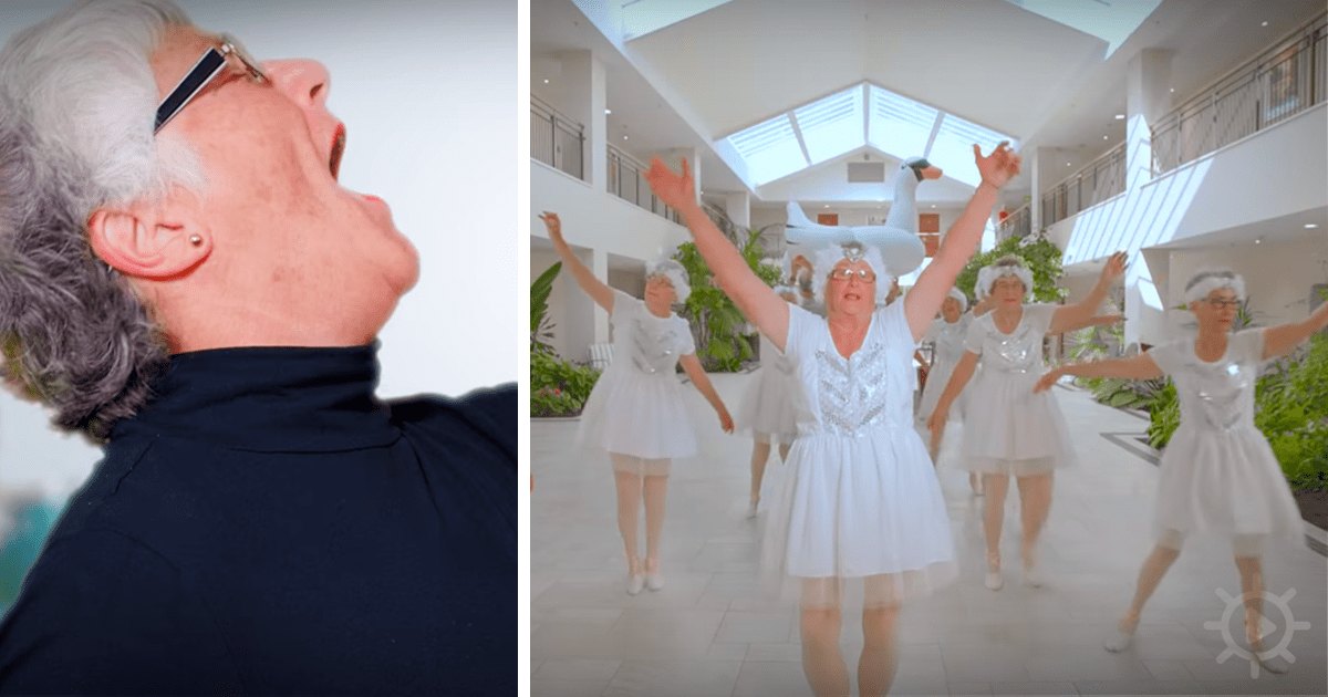 An older adult male with gray hair and glasses wearing a dark turtleneck shirt indoors; background includes white walls, skylight, plants, and a group of women in white tutus and ballet shoes suggesting a dance class or performance.