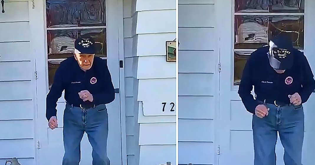 A middle-aged man wearing a U.S. Navy zip-up sweatshirt and jeans, standing outside near a house with white siding in clear daylight.