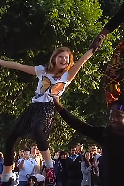 A street performer with a young adult female child in London, England, surrounded by onlookers and iconic Big Ben clock tower in the background during late afternoon or early evening.