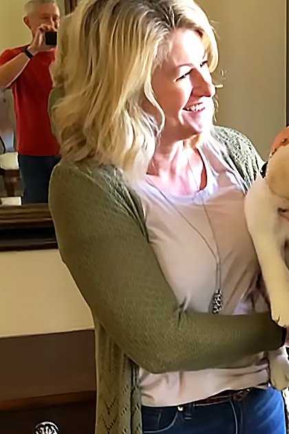 A golden retriever puppy being held between two women indoors with natural daylight filtering through a window.