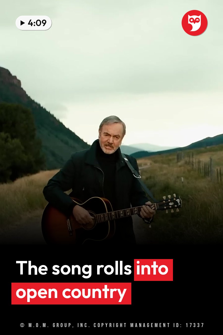 Neil Diamond plays an acoustic guitar on a grassy field, with hills and a cloudy sky behind him. A headline runs in white letters across the lower third.