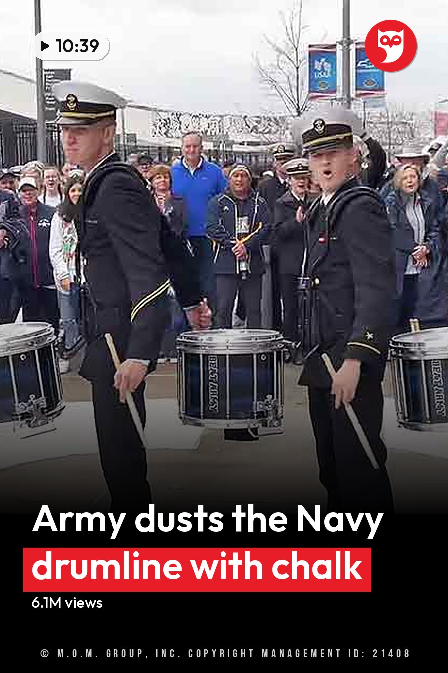 A marching band at an outdoor event near a stadium with young adult to middle-aged male and female members in military-style uniforms holding drumsticks. The headline runs in white letters across the lower third.