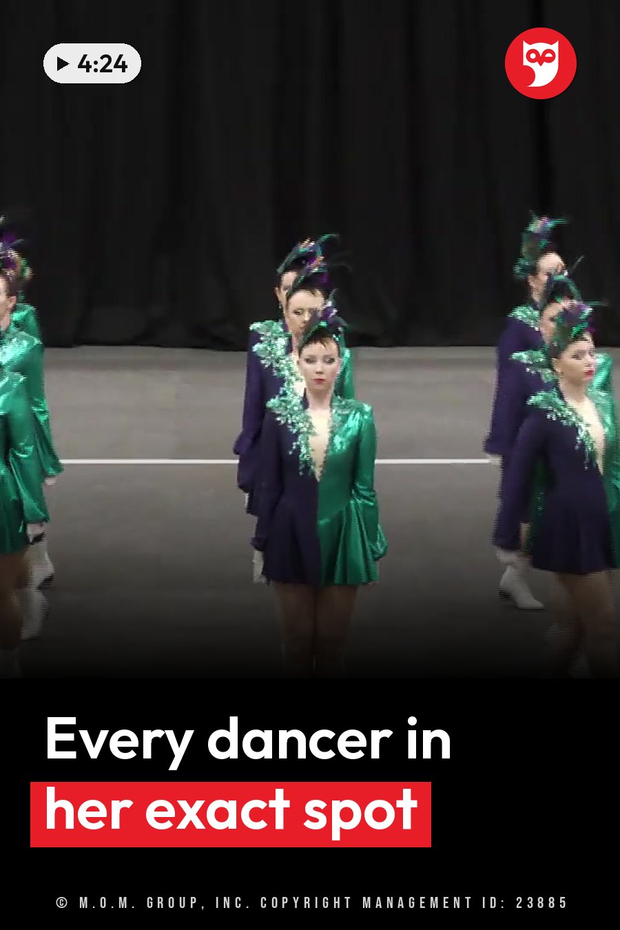Dancers in green and purple costumes with feathered headpieces stand on a stage during a performance. A headline runs in white letters across the lower third.