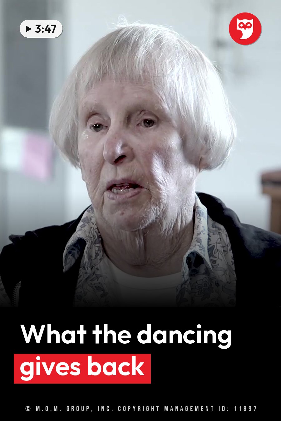 An elderly woman with white hair speaks, wearing a patterned shirt under a dark jacket. A headline runs in white letters across the lower third.