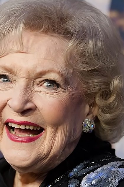 An older adult female wearing a black, form-fitting dress adorned with blue and silver sequins at what appears to be a public event or premiere.