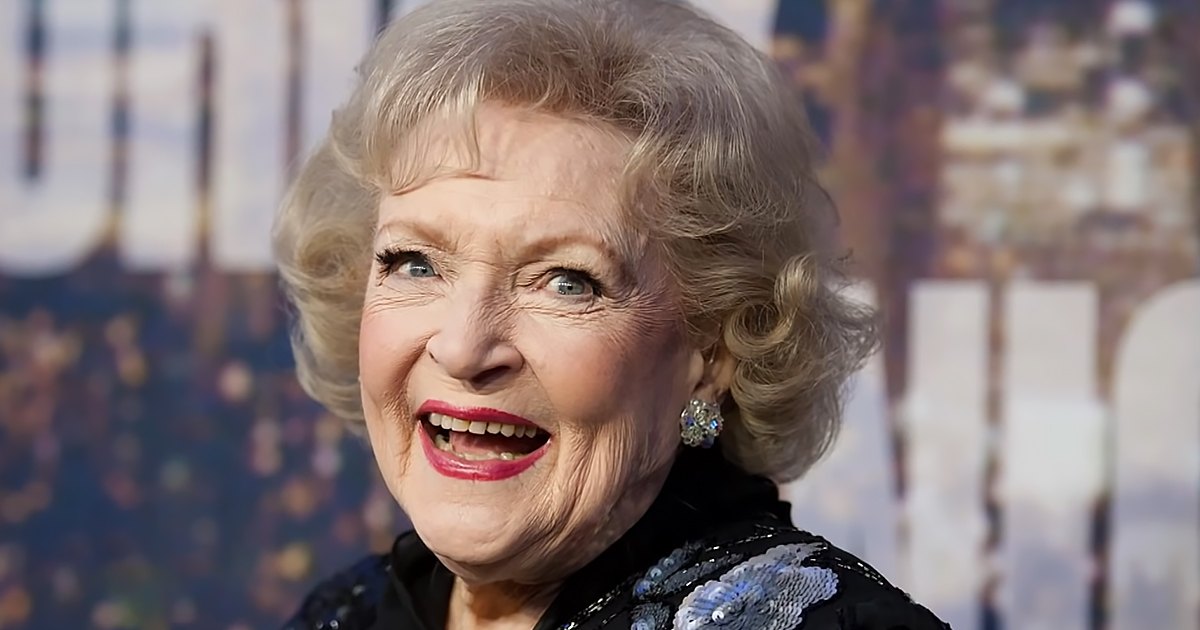 An older adult female wearing a black, form-fitting dress adorned with blue and silver sequins at what appears to be a public event or premiere.