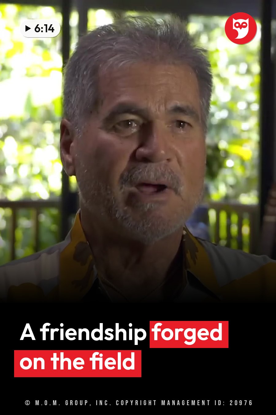A man with gray hair and a mustache speaks in a patterned shirt, seated indoors with greenery outside. A headline runs in white letters across the lower third.