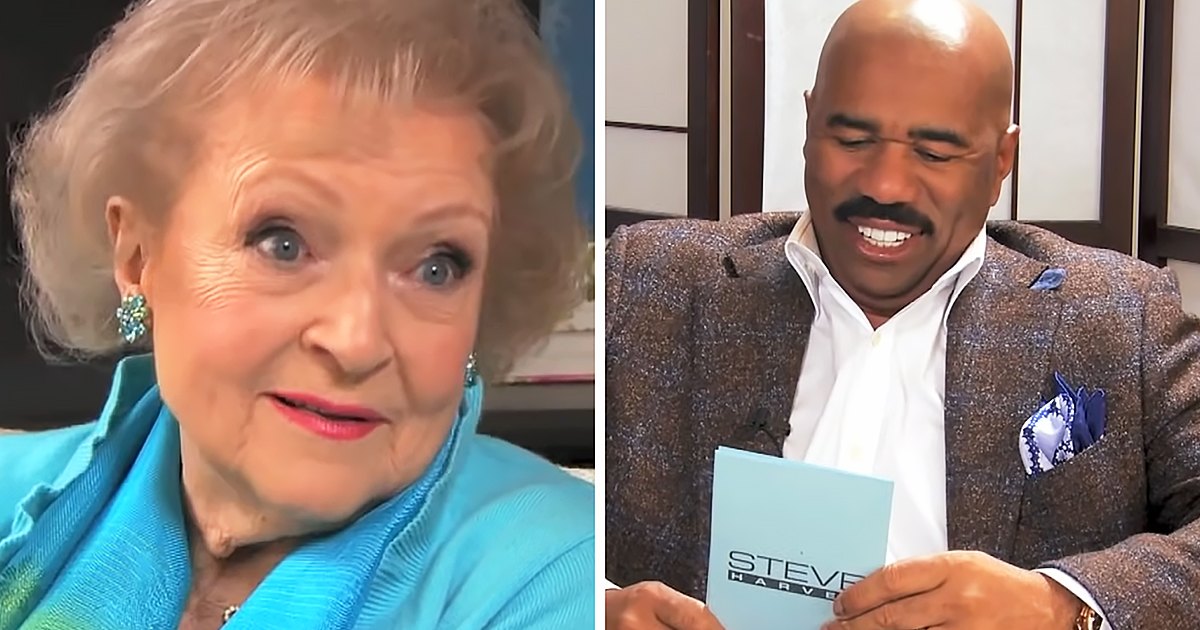 A middle-aged woman wearing a bright blue textured patterned blouse with large gemstone earrings, standing next to an adult male holding a card labeled 'STEVE HARVEY', in what appears to be an indoor studio or home office setting.