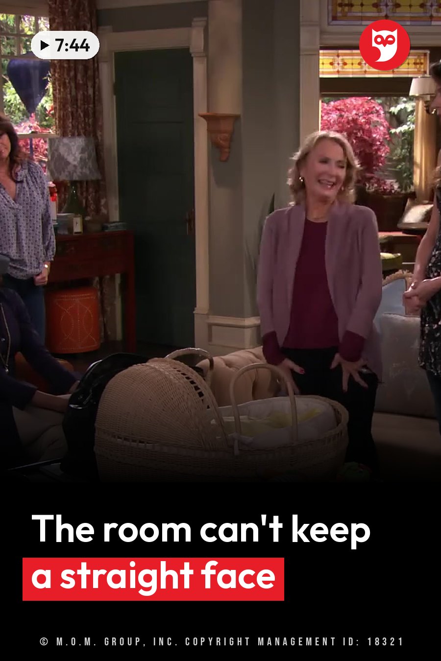 A woman laughs as she stands near a wicker bassinet in a furnished room with other people nearby. A headline runs in white letters across the lower third.
