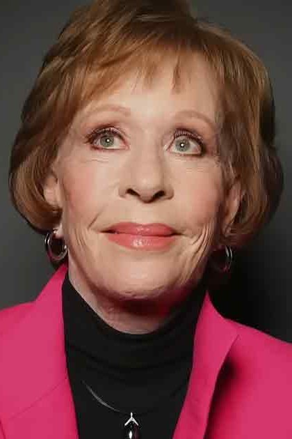 An older adult female wearing a bright pink blazer with notched lapels and black turtleneck, holding 'Madly Odd' text in a studio setting.