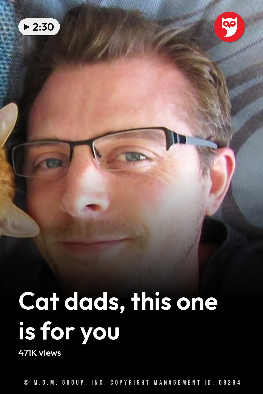An adult male wearing a dark gray t-shirt, lying with an orange tabby cat on blue patterned fabric in a home setting during daytime. The headline runs in white letters across the lower third.
