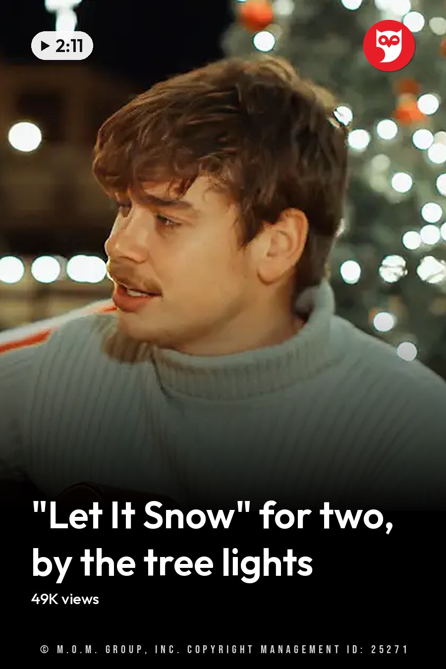 A couple singing in front of decorated Christmas trees at night, with a festive outdoor setting and artificial lighting creating a cozy holiday atmosphere. The headline runs in white letters across the lower third.