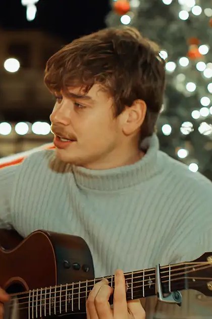 A couple singing in front of decorated Christmas trees at night, with a festive outdoor setting and artificial lighting creating a cozy holiday atmosphere.