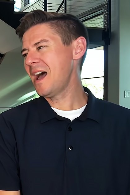Young adult female in a white lace blouse and young adult male in a dark blue polo shirt indoors, modern home setting with staircase and natural daylight.