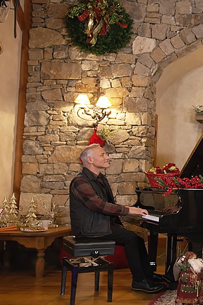 A cozy living room decorated for Christmas with a grand piano adorned with red berries, a lit tree, and festive decorations. The season is winter, indicated by the holiday-themed items and indoor lighting.