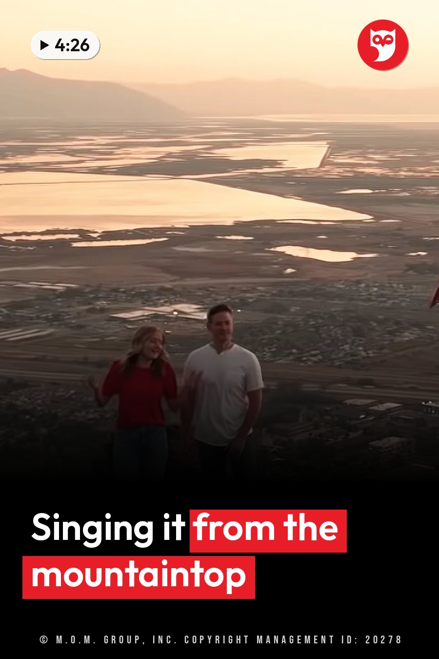 Two people stand on a high lookout above a wide landscape of water and distant mountains at sunset. A headline runs in white letters across the lower third.