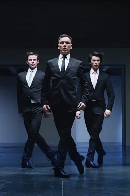 Group of individuals dressed in formal attire, standing indoors with a neutral background and even lighting.