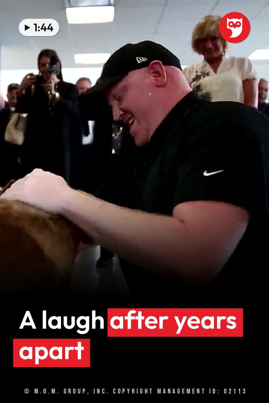 A man in a black cap and shirt laughs while petting a dog, surrounded by people watching and taking photos. A headline runs in white letters across the lower third.