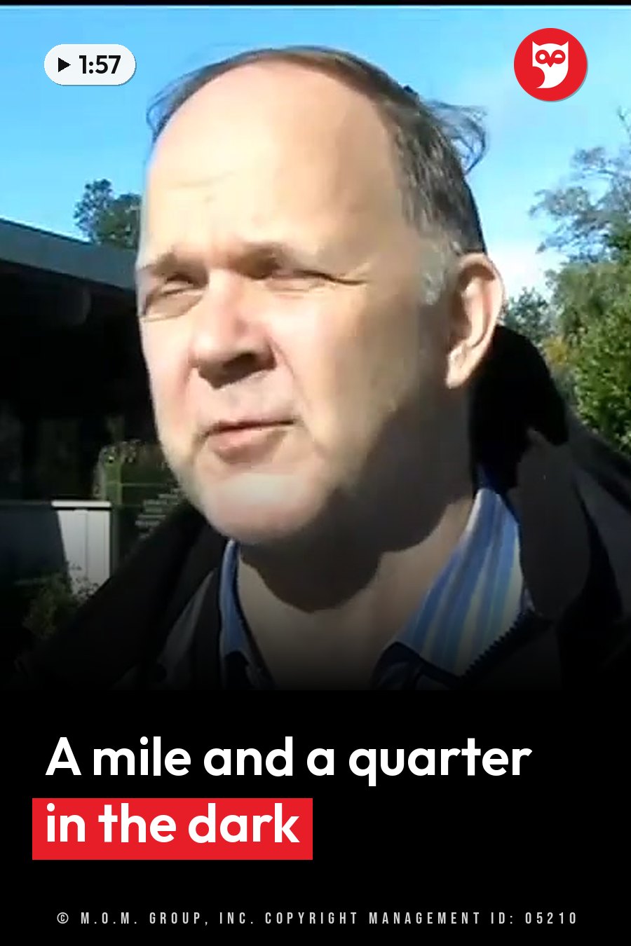 A man with thinning hair, in a dark jacket over a striped shirt, speaks outdoors under a clear blue sky. A headline runs in white letters across the lower third.