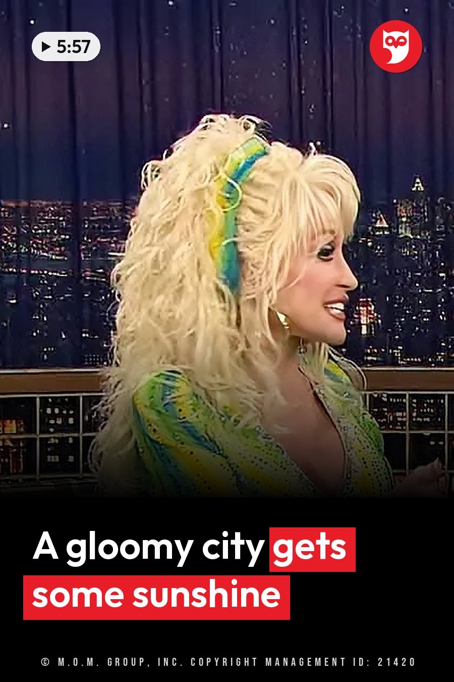 Dolly Parton, with long blonde hair and a colorful outfit, smiles in a chair in front of a city skyline backdrop at night. A headline runs in white letters across the lower third.