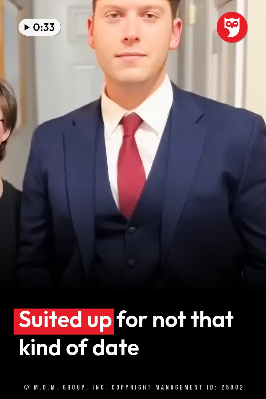 A man in a dark blue suit and red tie stands facing the camera in a home. A headline runs in white letters across the lower third.