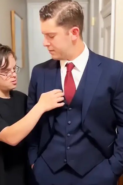 Two young adult males in a residential interior, wearing casual T-shirt and formal suit with red tie respectively.