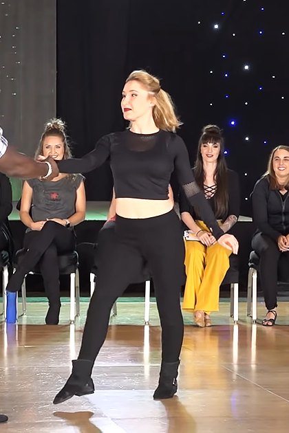 A dance performance at a studio or event space with participants in various settings and attire, including a man leading and a woman dancing.