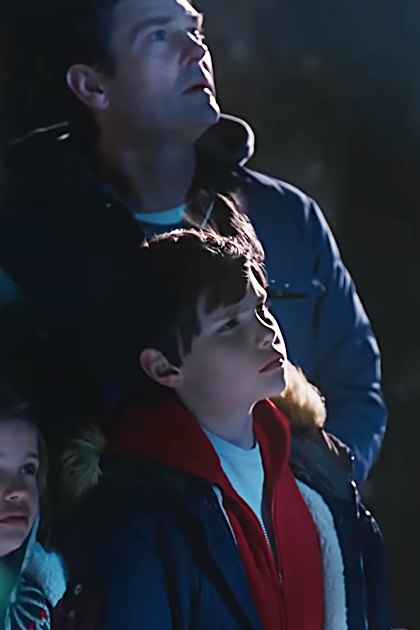 A family scene at night in an outdoor park-like area with trees and artificial lighting illuminating their faces.