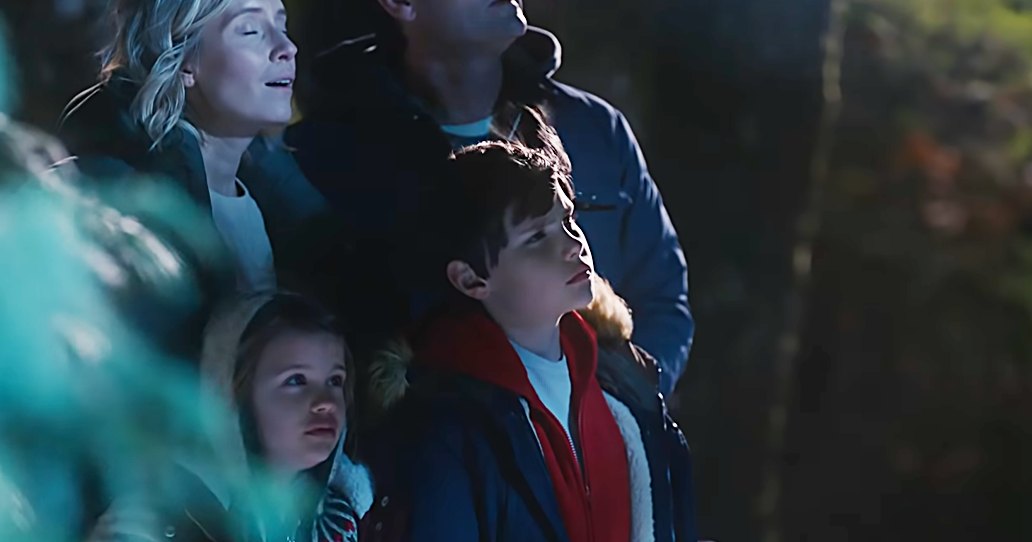 A family scene at night in an outdoor park-like area with trees and artificial lighting illuminating their faces.