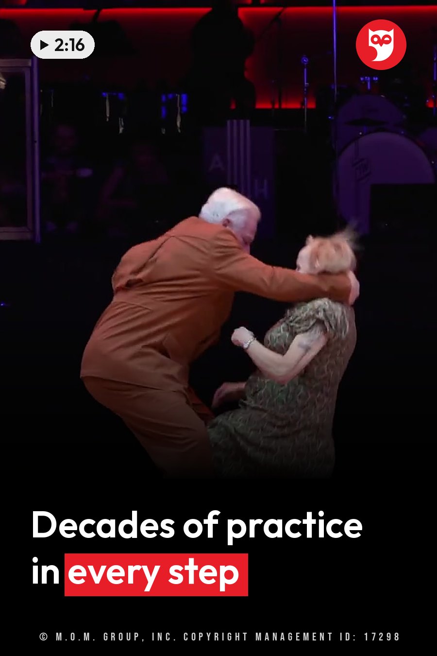 An older man and woman dance close together on a dim stage lit in red. A headline runs in white letters across the lower third.