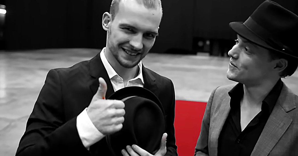 Two young adult males in a casual indoor setting, wearing formal attire; red carpet suggests an event space.