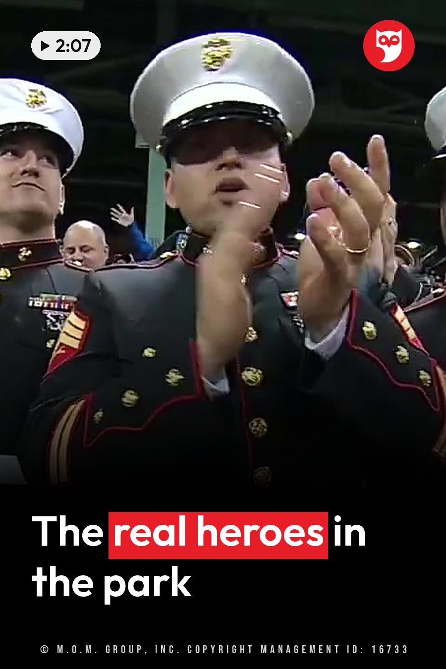 Men in ceremonial dress uniforms applaud with their hands raised. A headline runs in white letters across the lower third.
