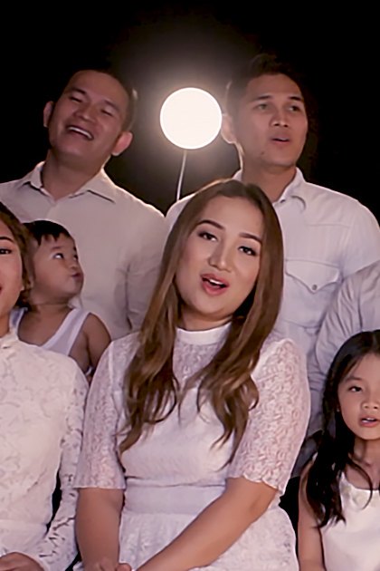 A family portrait in a studio setting with adults and children wearing white outfits, professional lighting and black background.