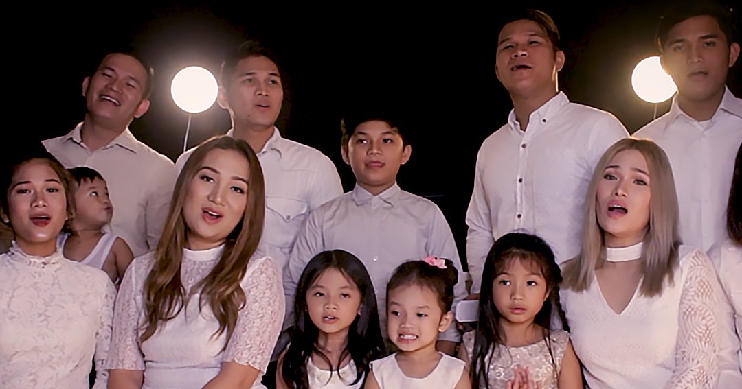 A family portrait in a studio setting with adults and children wearing white outfits, professional lighting and black background.