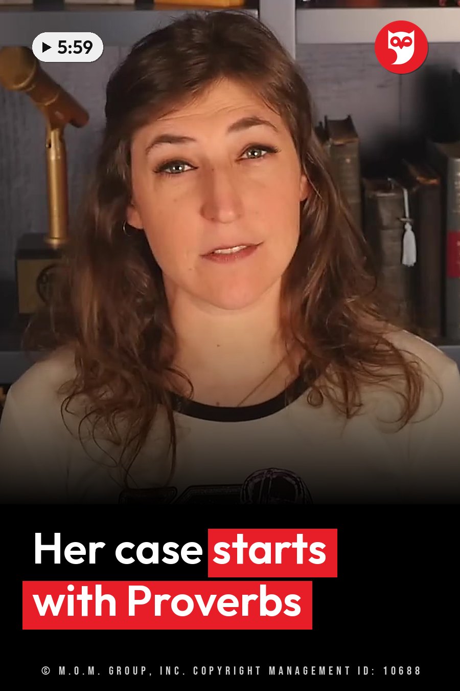 Mayim Bialik, in a white shirt with black trim, sits in front of bookshelves and a microphone. A headline runs in white letters across the lower third.