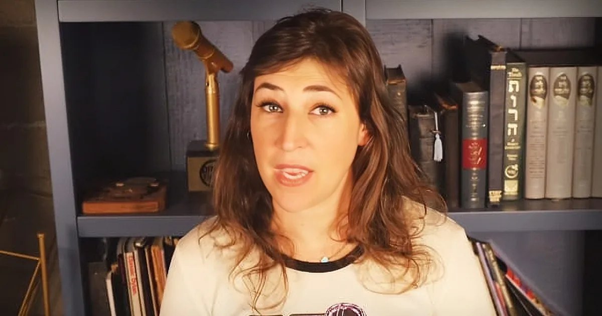 A young adult female wearing a white long-sleeved t-shirt with Darth Vader graphic in an indoor home office setting.