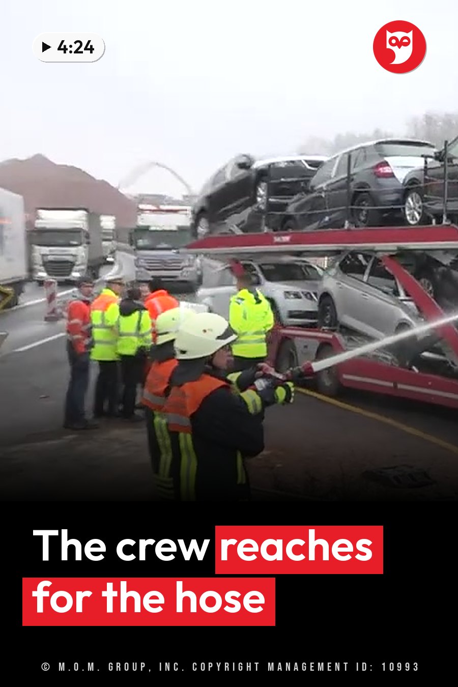 Firefighters spray water toward a car carrier truck stacked with cars on a wet road. A headline runs in white letters across the lower third.