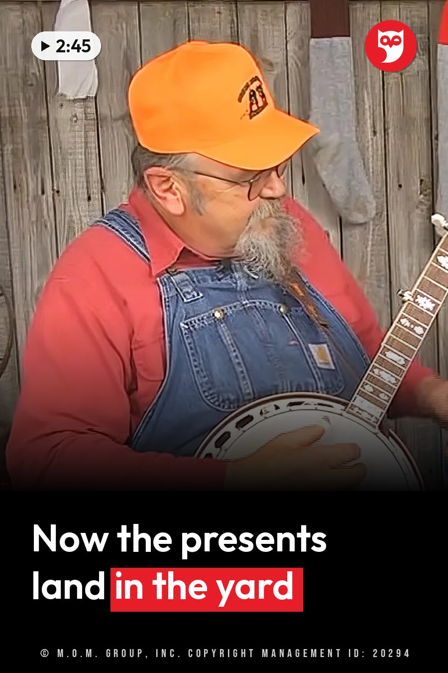 A man in an orange cap and overalls plays a banjo in front of a wooden fence. A headline runs in white letters across the lower third.