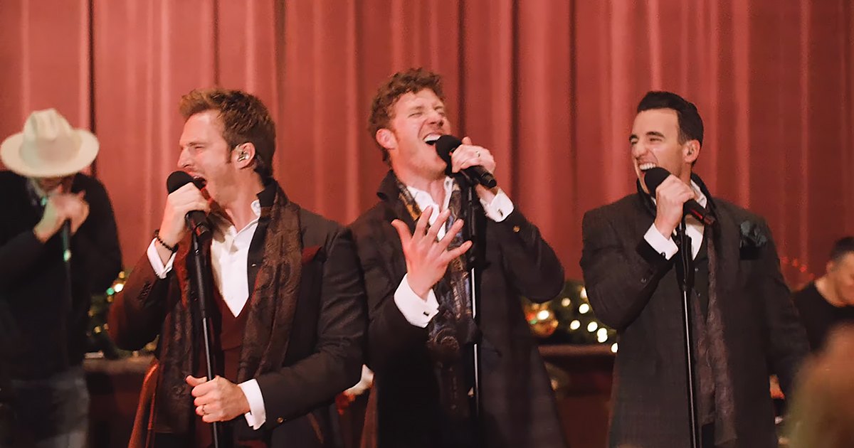 Group performance scene at an indoor event, possibly a concert or holiday celebration with formal attire and festive decor.