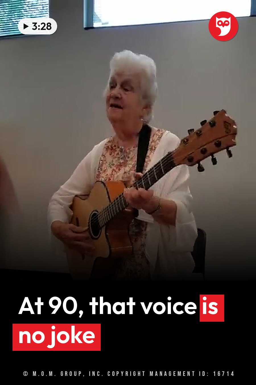 Vera, wearing a floral top and a white cardigan, sings while playing an acoustic guitar. A headline runs in white letters across the lower third.