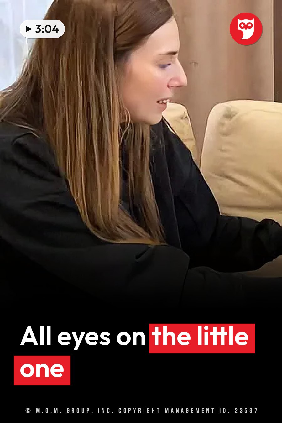 A woman with long brown hair in black clothing sits on a couch, looking down at something in her hands. A headline runs in white letters across the lower third.