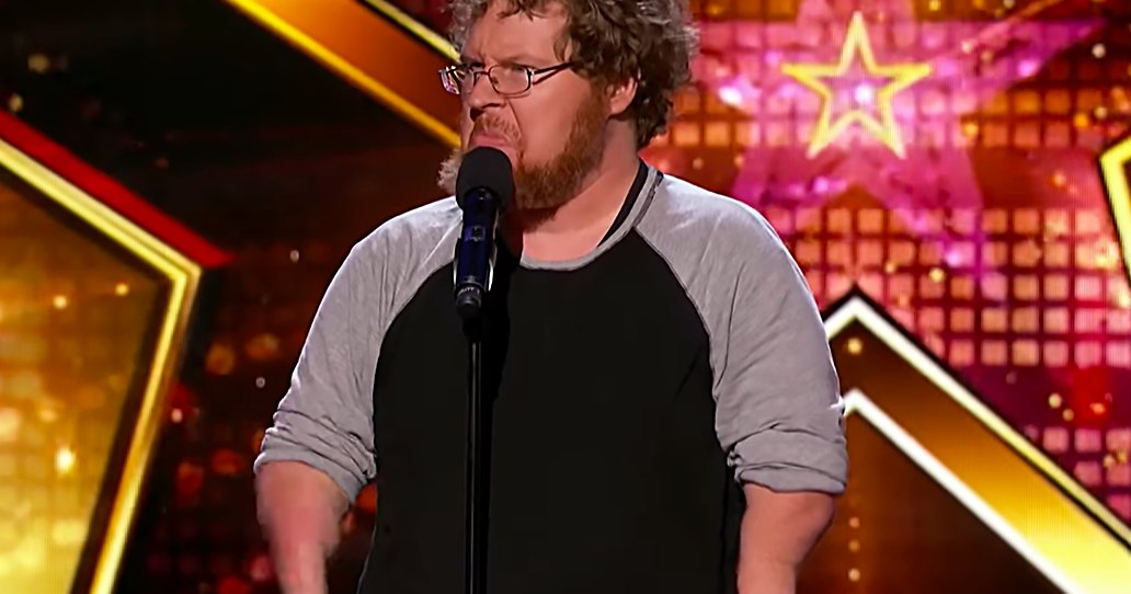 A middle-aged adult male wearing a long-sleeved raglan shirt with a relaxed fit and crew neck, performing on stage at an entertainment competition show.