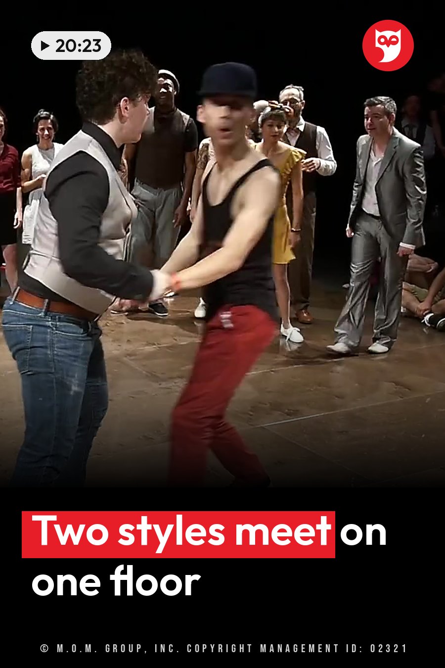 Two men dance on a stage while others watch from behind; one wears red pants and a cap, the other jeans and a vest. A headline runs in white letters across the lower third.
