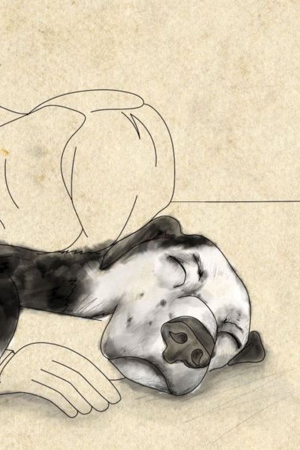 Adult male wearing a light-colored, loose-fitting shirt lying with a black-and-white Boxer dog on parchment paper in an indoor setting.