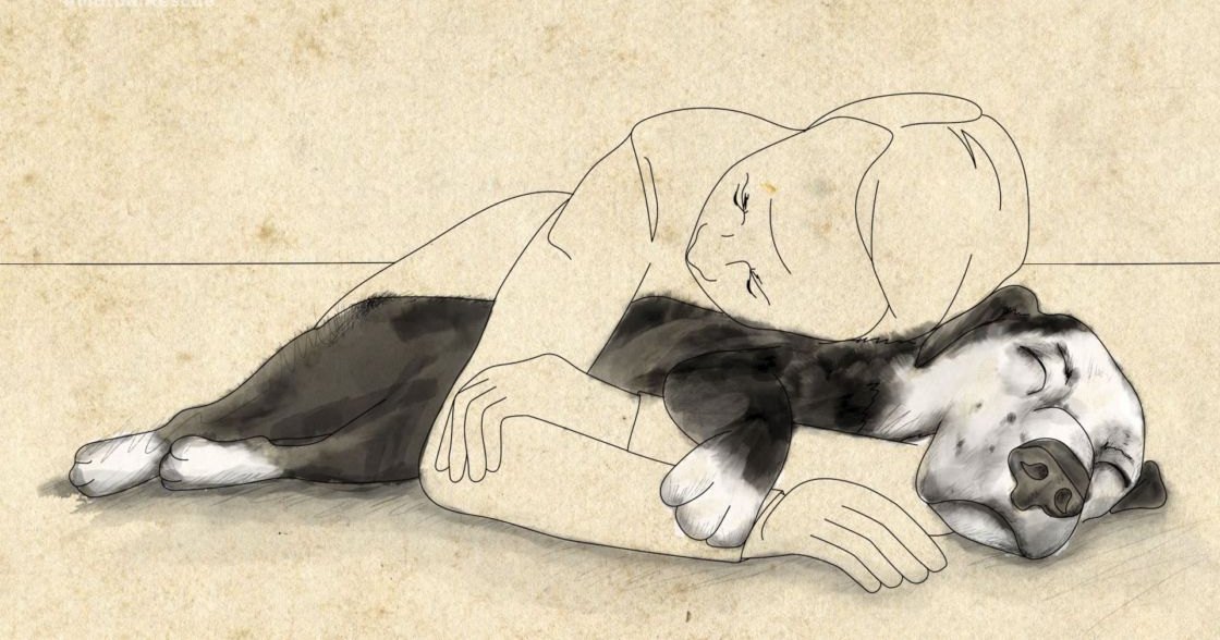 Adult male wearing a light-colored, loose-fitting shirt lying with a black-and-white Boxer dog on parchment paper in an indoor setting.