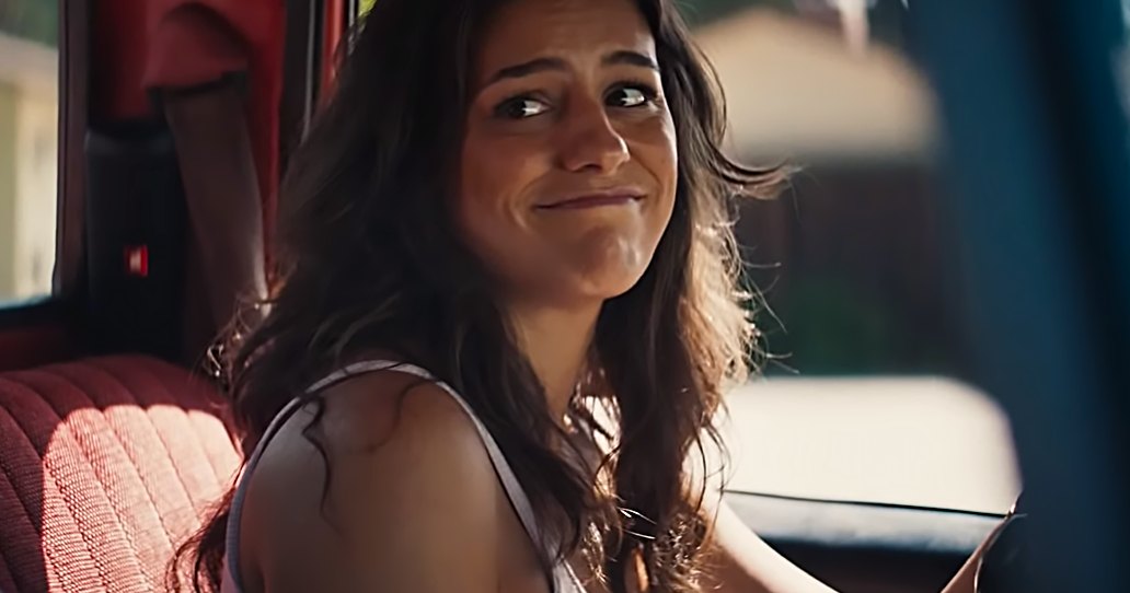 Young adult to middle-aged woman in a white tank top inside a vehicle with red seat, modern steering wheel design, logo on seat reading 'H', daytime car interior setting.